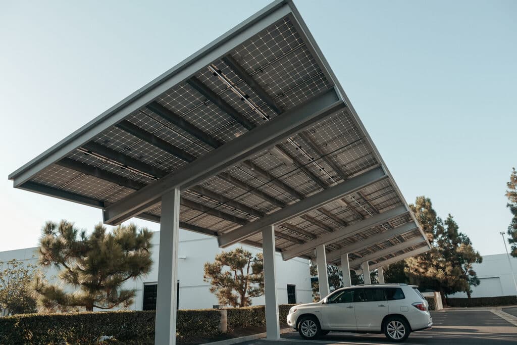 Unteransicht eines Photovoltaik-Carports mit Solarmodulen auf Stahlkonstruktion, darunter geparkter Pkw auf einem gewerblichen Parkplatz.
